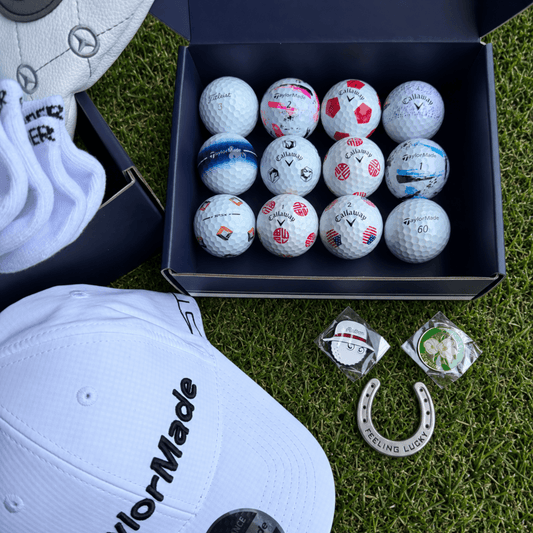 Overhead view of twelve golf balls in the Presidential box tray with a TaylorMade cap, glove and ball markers on grass