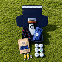 Members Mystery Box on grass: navy Clubhouse Goods box with a Titleist glove, golf balls, tees and sweets