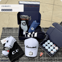 Presidential box accessories laid out on grass: a white driver headcover, golf balls, gift boxes, towel and tees