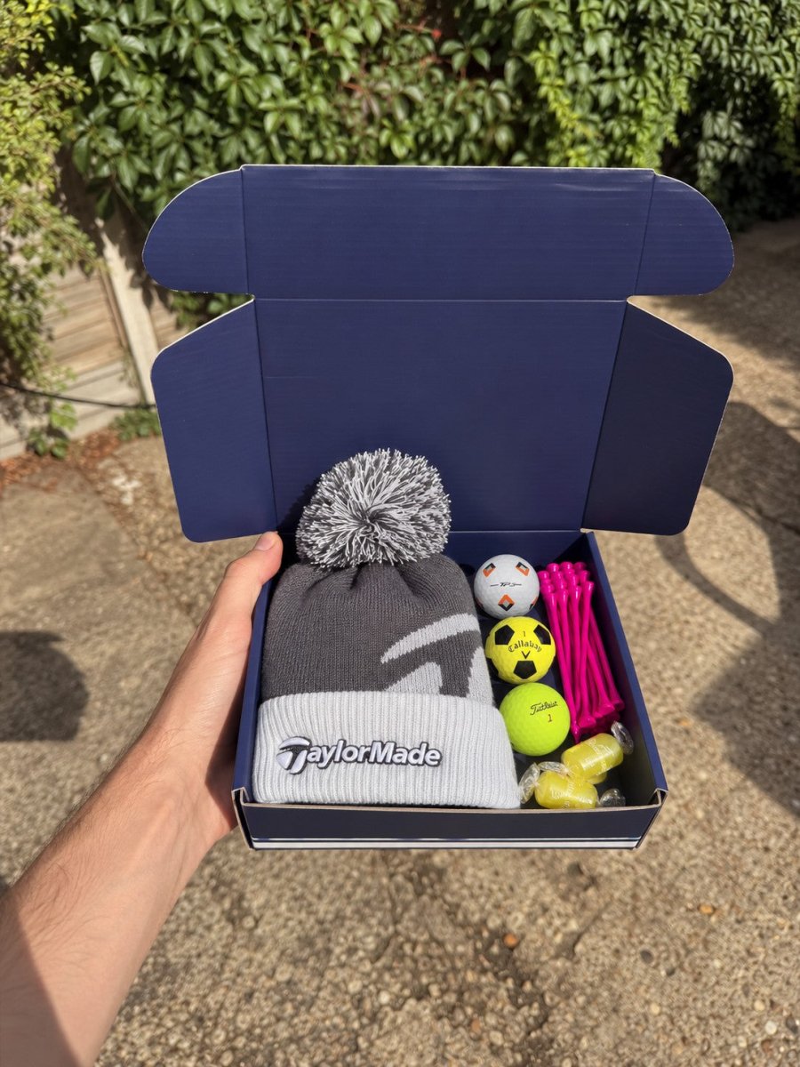 The Winter Caddie golf gift box with a grey TaylorMade bobble beanie, three golf balls, hot pink tees and sherbet lemons