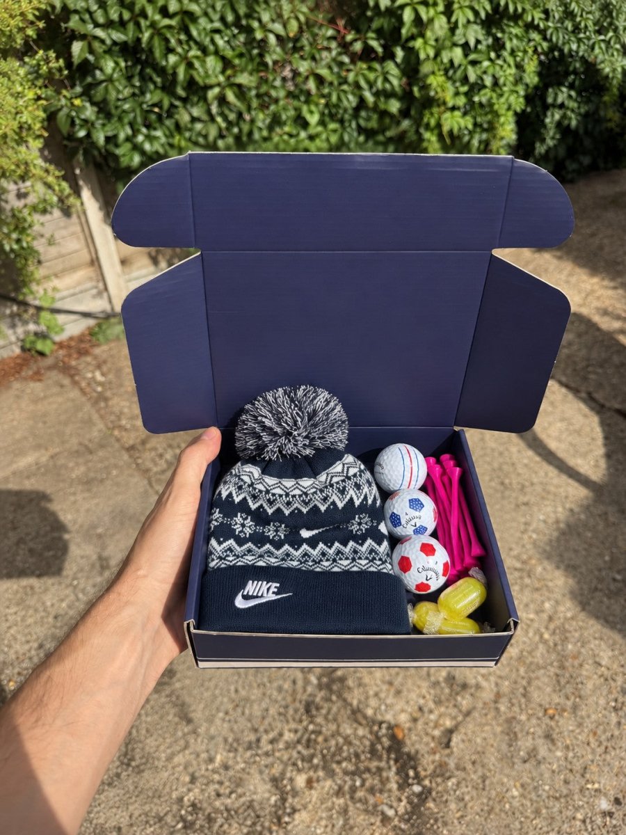The Winter Caddie golf gift box held open: a navy Nike bobble beanie, three golf balls, hot pink tees and sherbet lemons